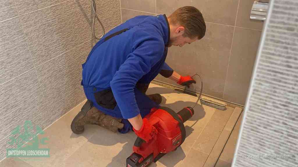 Een monteur ontstopt een langwerpige douchegoot met een elektrische veer, een doucheputje verstopt door haren en zeep in Leidschendam