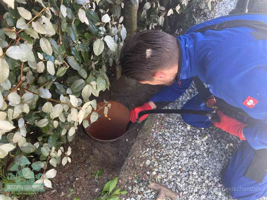 Een monteur voert een slang in een geopende rioolput in de tuin om het hoofdriool te ontstoppen in Leidschendam