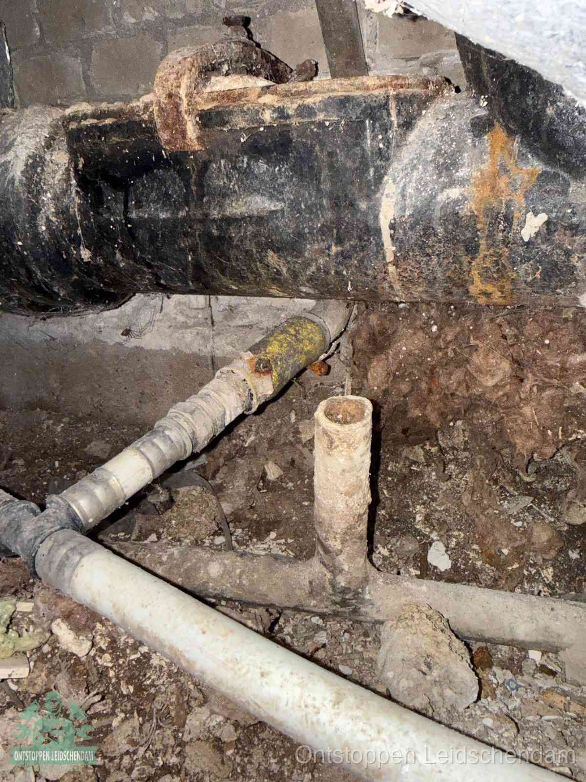 Een oude hoofdrioolbuis met roest- en kalkaanslag in een kruipruimte, oorzaak van terugkerende structurele rioolproblemen in Leidschendam
